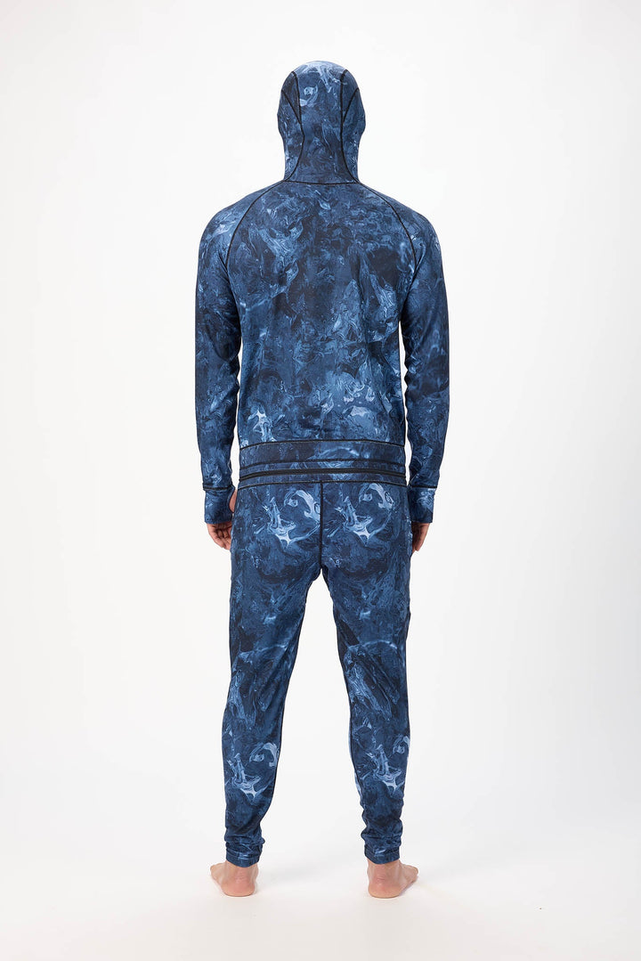 behind view A man wearing a blue swirl patterned onesie with a hooded with a zipper and jogger pants, standing against a plain white studio background.