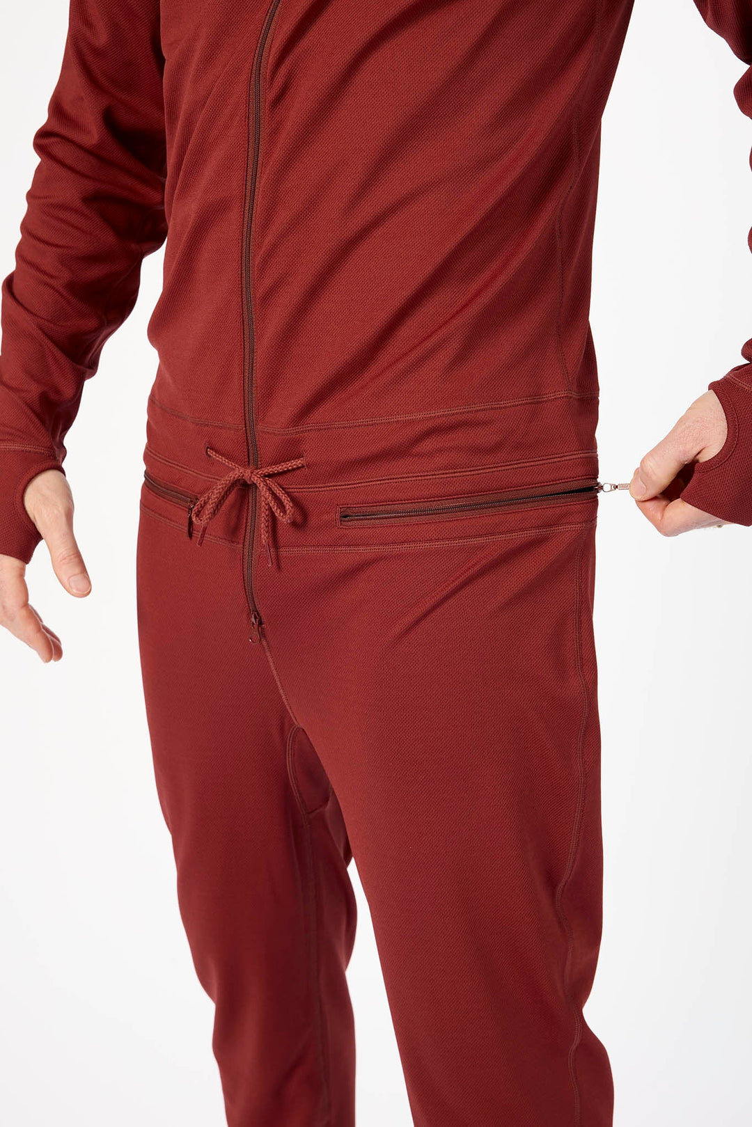 A close-up of a person wearing a matching burgundy zip-up jacket and jogger pants set, showing the waistband with a drawstring and a zippered pocket on the pants.