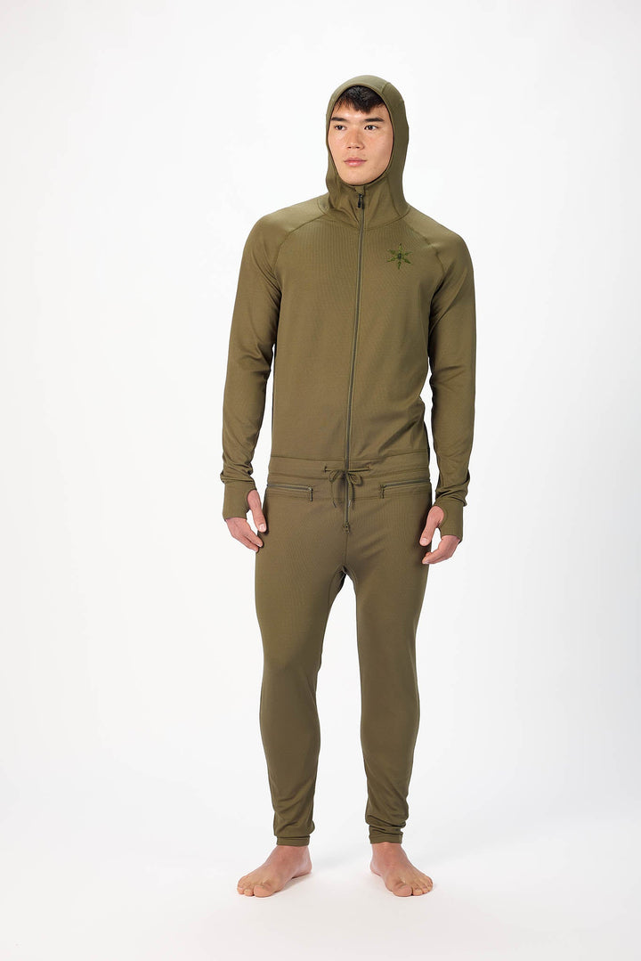 A man wearing a Olive  onesie with a hooded with a zipper and jogger pants, standing against a plain white studio background.