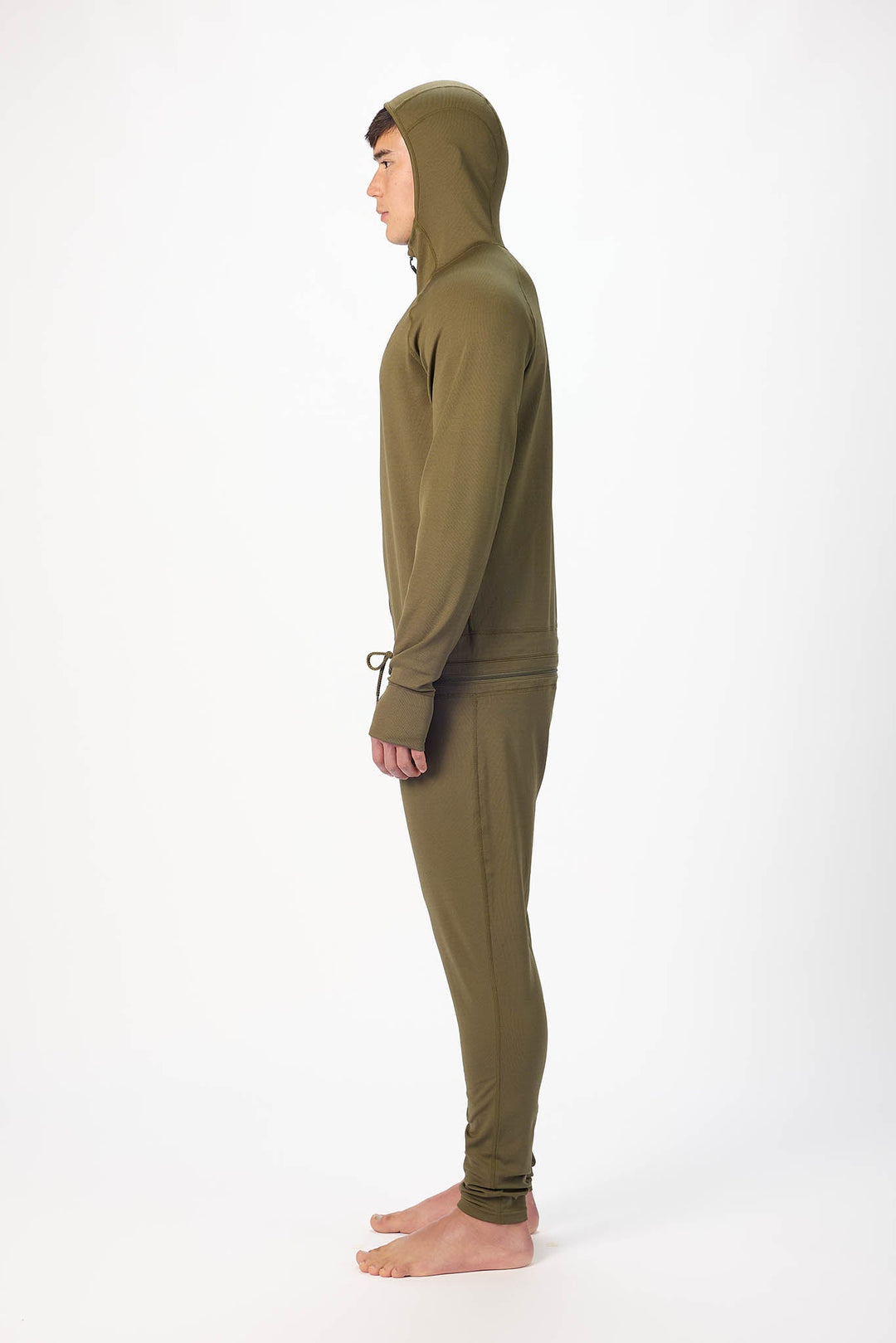 side profile of a man wearing a Olive  onesie with a hooded with a zipper and jogger pants, standing against a plain white studio background.