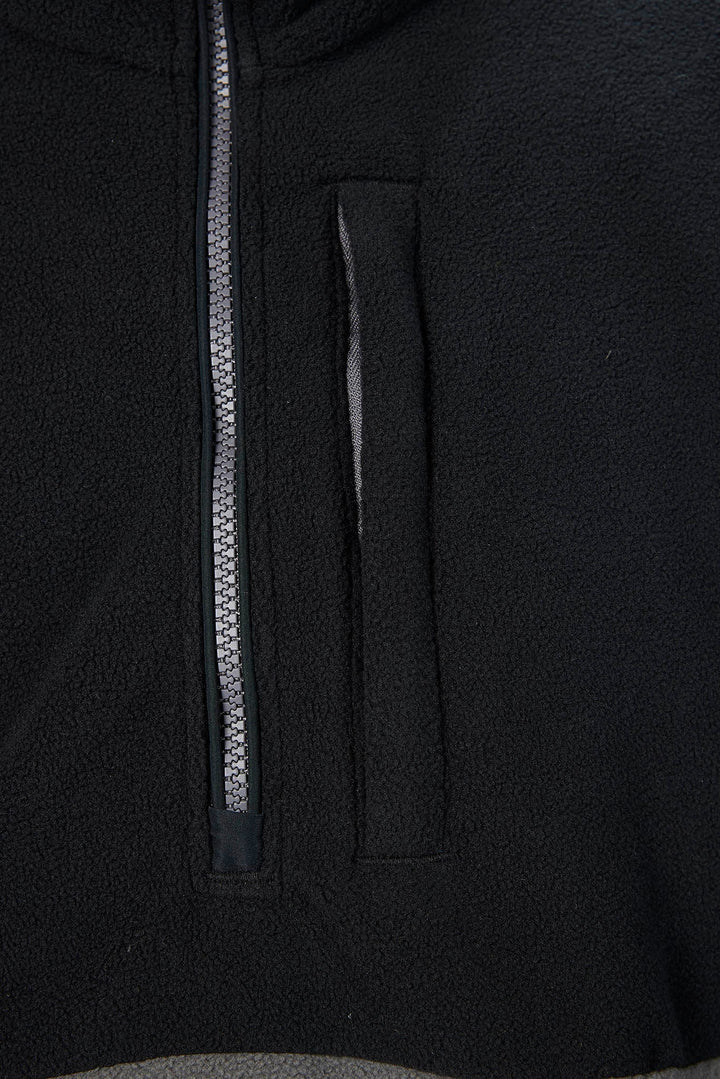 Close-up of a black fleece jacket showing a vertical front zipper and a side zip pocket.