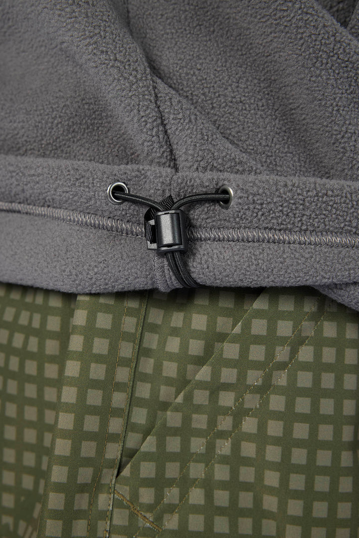 Close-up of a gray fleece garment with a black drawstring toggle, layered over an olive green and beige checkered fabric.