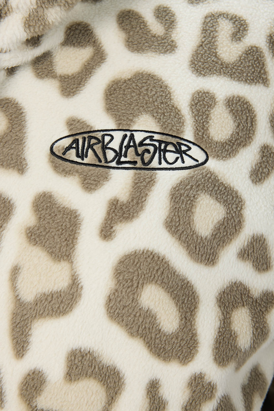 Close-up of a plush fleece fabric with a beige and brown leopard print pattern and a black embroidered oval logo reading AIRBLASTER.