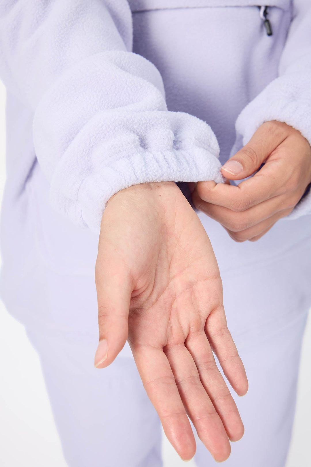 A close-up of a person wearing a light lavender fleece tracksuit, showing the ribbed elastic cuff of the long-sleeve top being adjusted by the hands.