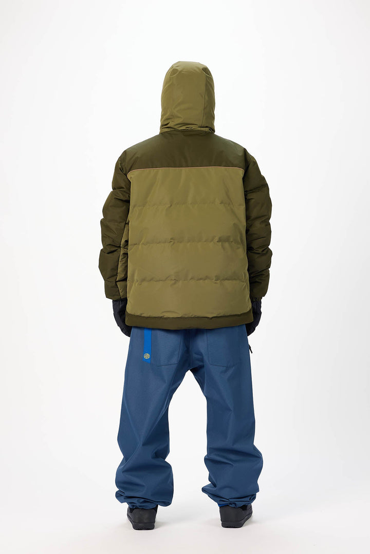 Person wearing a green and brown insulated jacket with blue pants on a white background