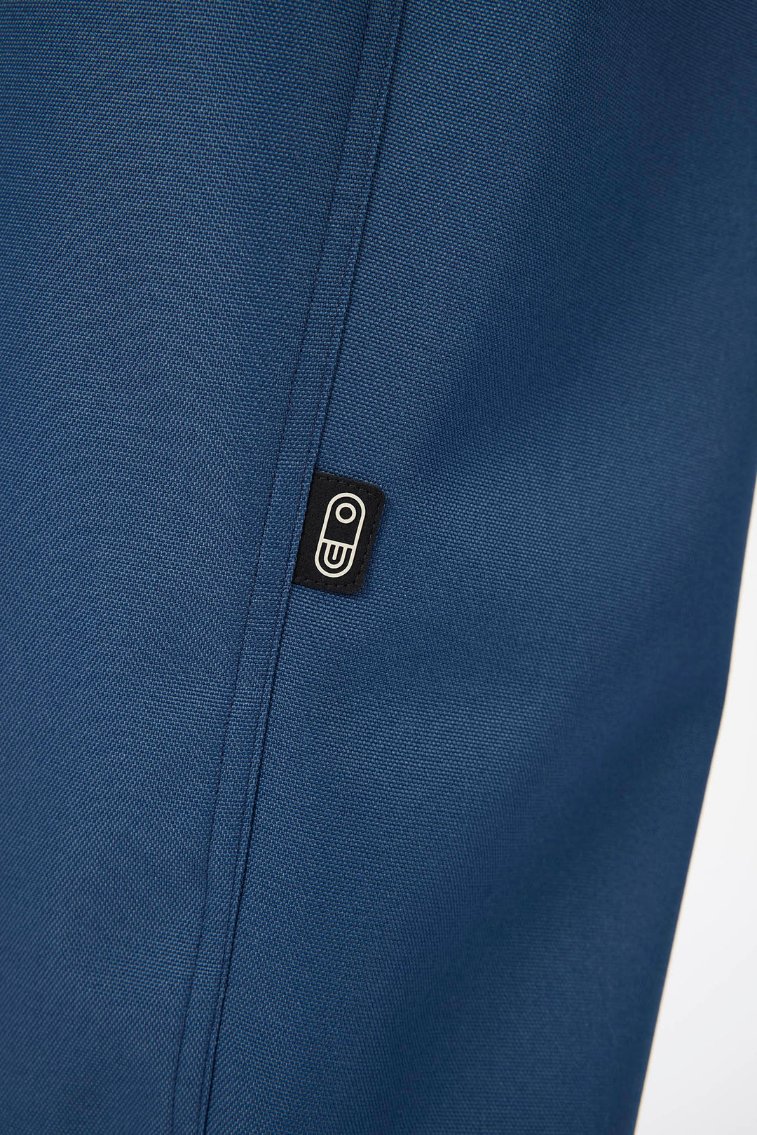 Close-up of a textured navy blue fabric with a small black rectangular brand patch featuring a white stylized &