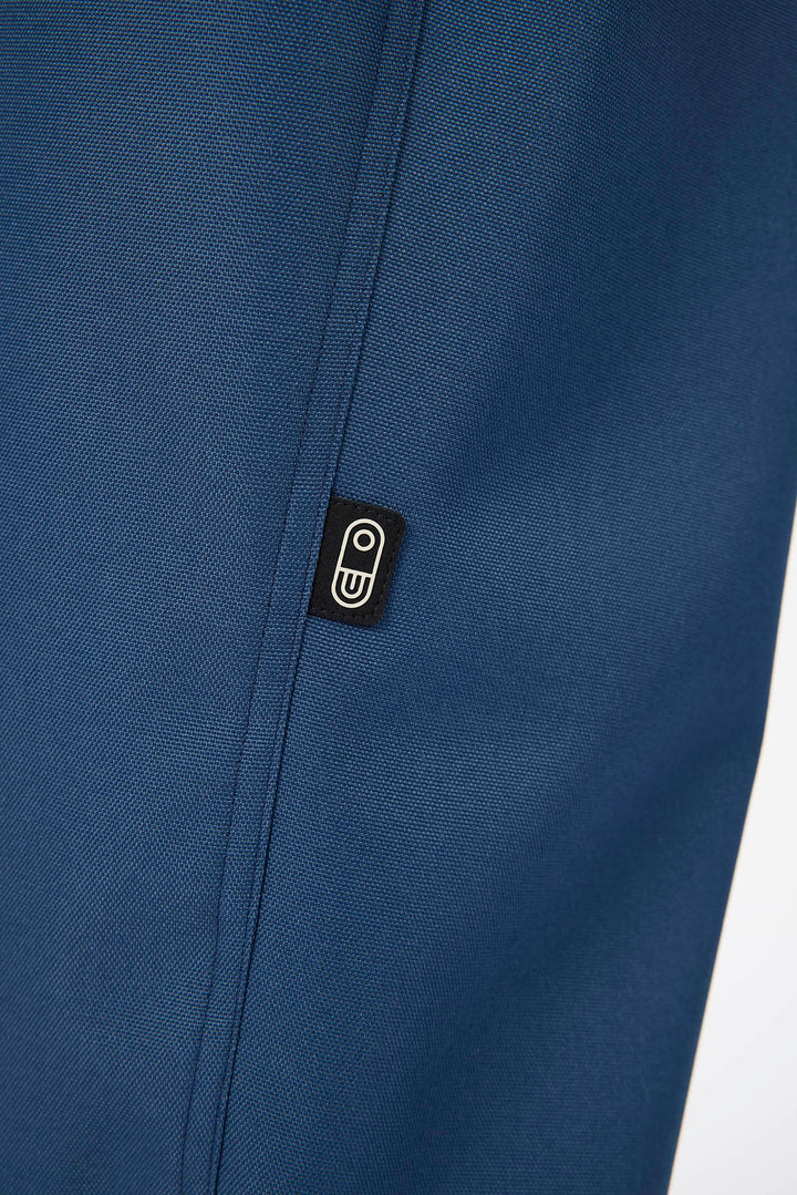 Close-up of a textured navy blue fabric with a small black rectangular brand patch featuring a white stylized &