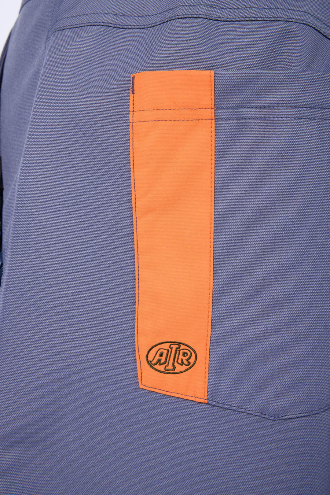 Close-up of a blue-gray fabric garment featuring a vertical orange pocket panel with an embossed circular &