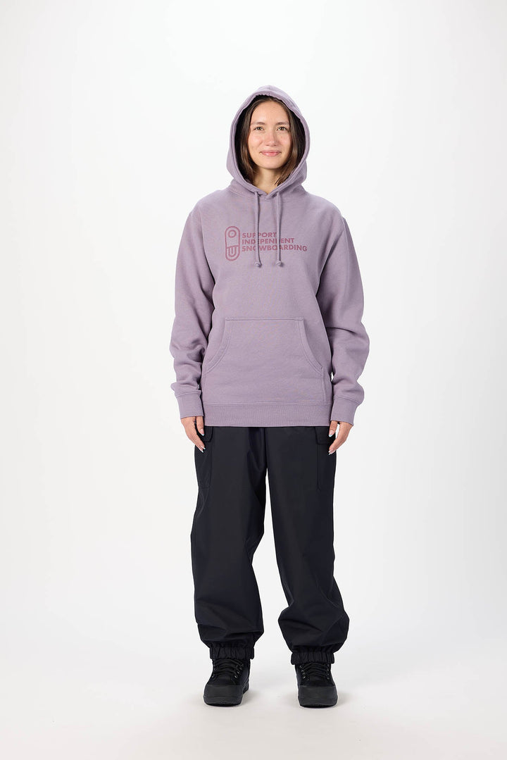A model wearing a lavender-purple pullover hoodie with a pink graphic logo on the chest, paired with black sweatpants and black sneakers, standing against a plain white studio background.