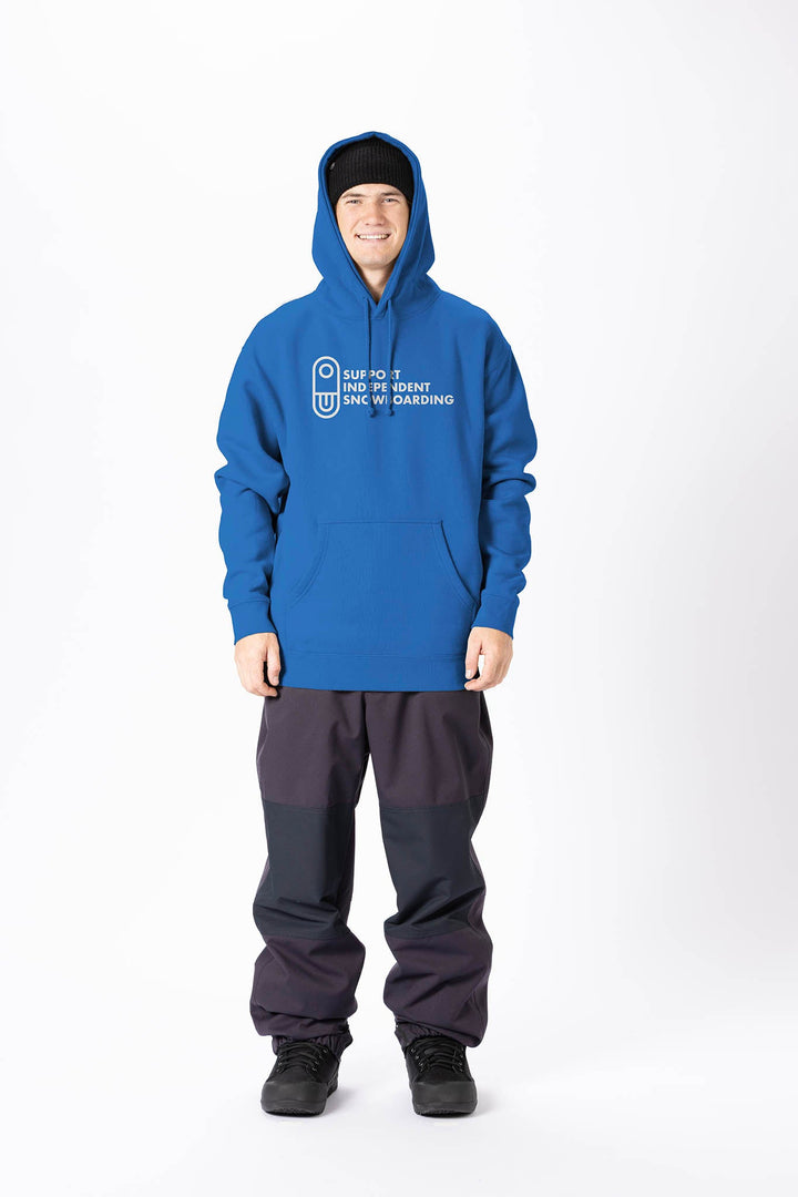 A man wearing a blue pullover hoodie with a white printed graphic on the chest, paired with dark gray and black pants, standing against a plain white studio background. 