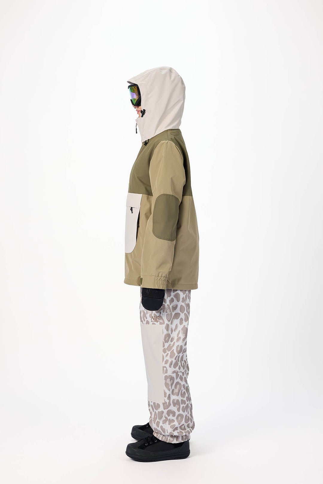 Person wearing a green and beige jacket with a white hood, standing against a white background.